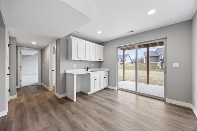kitchen featuring white cabinets, light countertops, baseboards, and wood finished floors