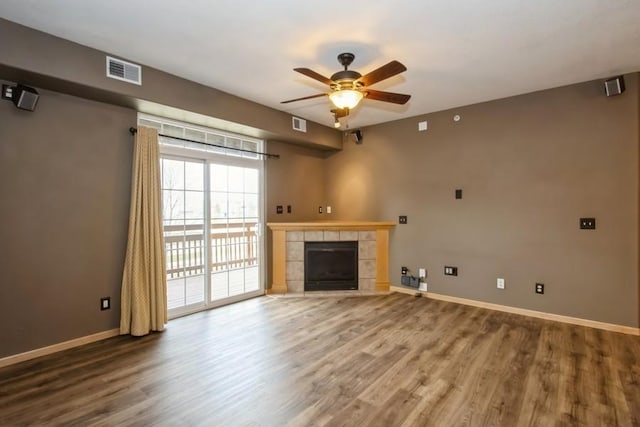 unfurnished living room featuring a tile fireplace, wood finished floors, baseboards, visible vents, and ceiling fan