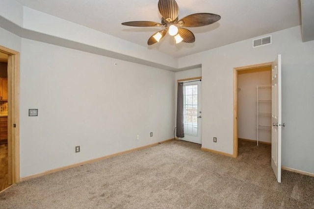 unfurnished bedroom featuring light colored carpet, a spacious closet, baseboards, a raised ceiling, and visible vents