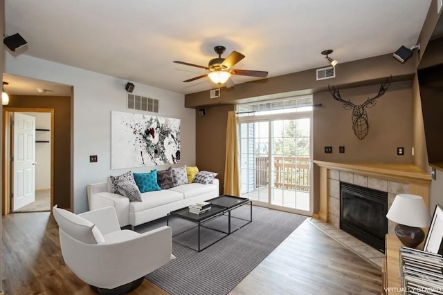 living room featuring a ceiling fan, a tile fireplace, wood finished floors, and visible vents