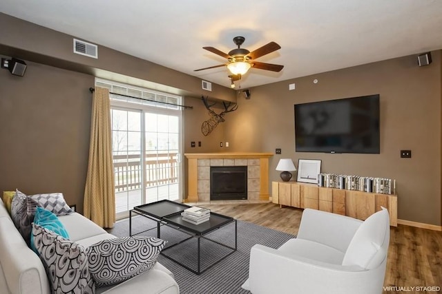 living room featuring a fireplace, wood finished floors, baseboards, visible vents, and ceiling fan