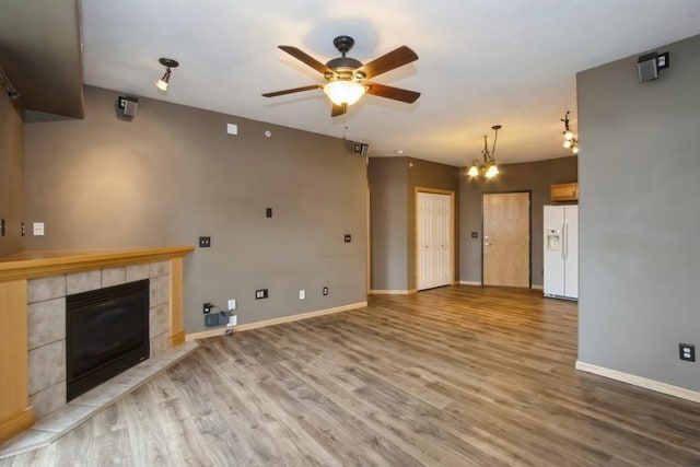 unfurnished living room featuring a tiled fireplace, ceiling fan with notable chandelier, baseboards, and wood finished floors