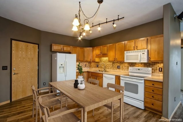 kitchen featuring light countertops, tasteful backsplash, white appliances, dark wood-type flooring, and a sink