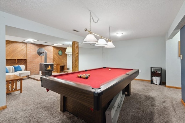 rec room with wooden walls, a textured ceiling, carpet floors, a wood stove, and visible vents