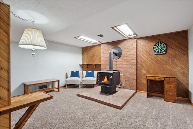 living area featuring visible vents, a wood stove, carpet, a textured ceiling, and wood walls