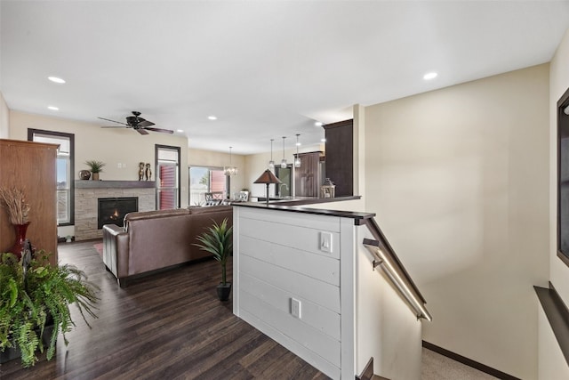 kitchen with dark brown cabinetry, recessed lighting, dark countertops, a stone fireplace, and a ceiling fan