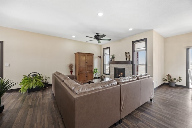 living area with baseboards, recessed lighting, dark wood-type flooring, a ceiling fan, and a stone fireplace