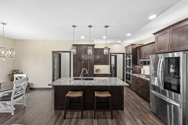 kitchen featuring dark brown cabinetry, appliances with stainless steel finishes, a sink, dark wood-style floors, and a center island with sink
