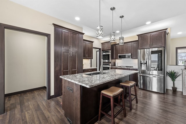 kitchen featuring a sink, stainless steel appliances, decorative backsplash, dark brown cabinetry, and an island with sink