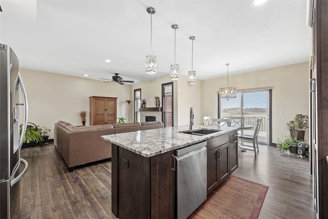 kitchen featuring a sink, stainless steel appliances, a fireplace, dark brown cabinets, and ceiling fan with notable chandelier