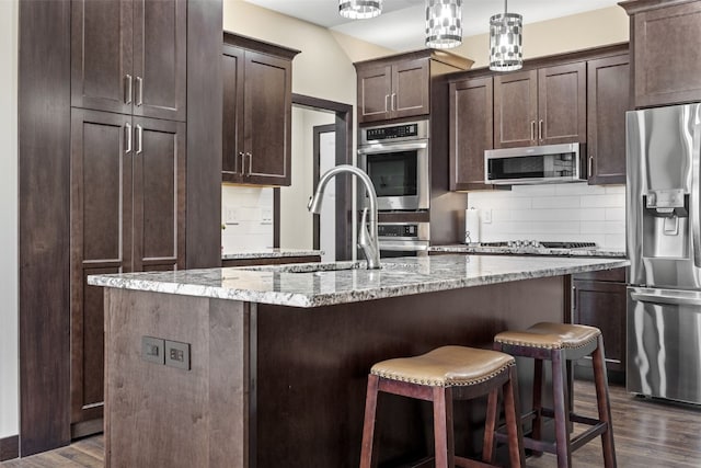 kitchen with dark brown cabinetry, backsplash, appliances with stainless steel finishes, and dark wood-type flooring