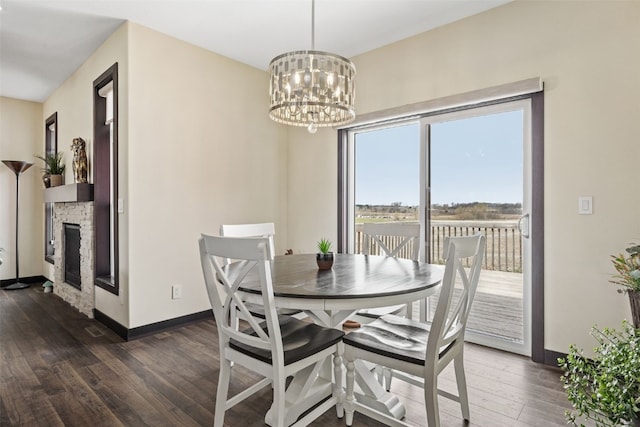 dining room with a stone fireplace, a notable chandelier, baseboards, and dark wood finished floors