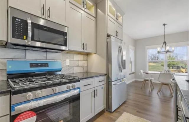 kitchen with tasteful backsplash, glass insert cabinets, decorative light fixtures, light wood-style floors, and stainless steel appliances