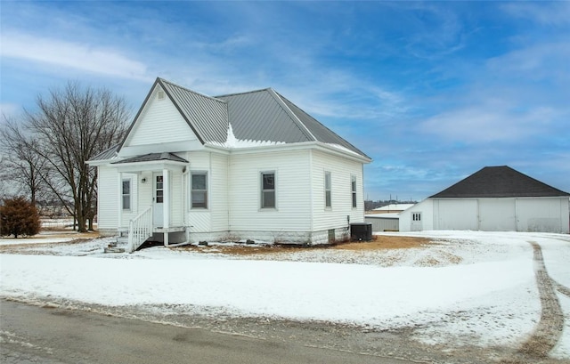 110 SE 12th St, Oelwein, IA 50662 - snow covered property featuring central air condition unit, a detached garage, an outdoor structure, metal roof, and a barn