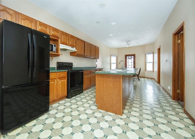 110 SE 12th St, Oelwein, IA 50662 - kitchen featuring baseboards, an island with sink, under cabinet range hood, black appliances, and light floors