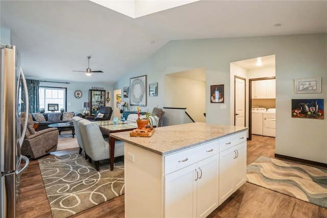 kitchen featuring lofted ceiling, wood finished floors, freestanding refrigerator, washing machine and clothes dryer, and white cabinets