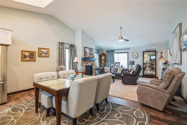 living area featuring vaulted ceiling, a stone fireplace, a ceiling fan, and wood finished floors