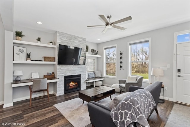 living area featuring a stone fireplace, baseboards, recessed lighting, ceiling fan, and wood finished floors