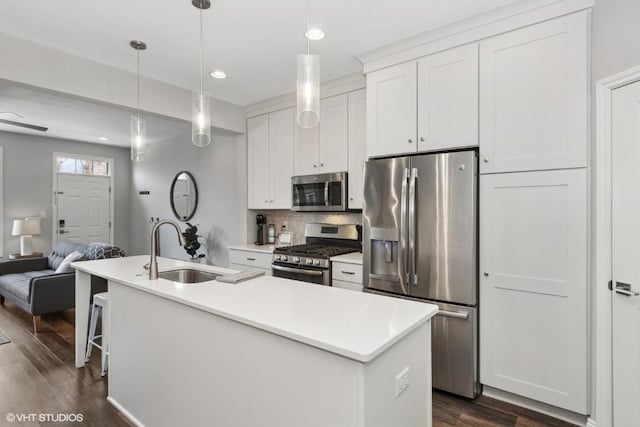 kitchen featuring tasteful backsplash, a sink, a kitchen island with sink, dark wood finished floors, and stainless steel appliances