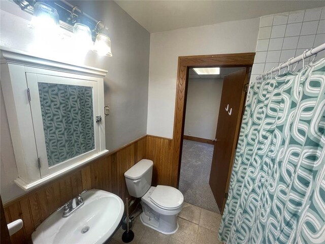 full bathroom featuring toilet, wood walls, a sink, wainscoting, and tile patterned floors