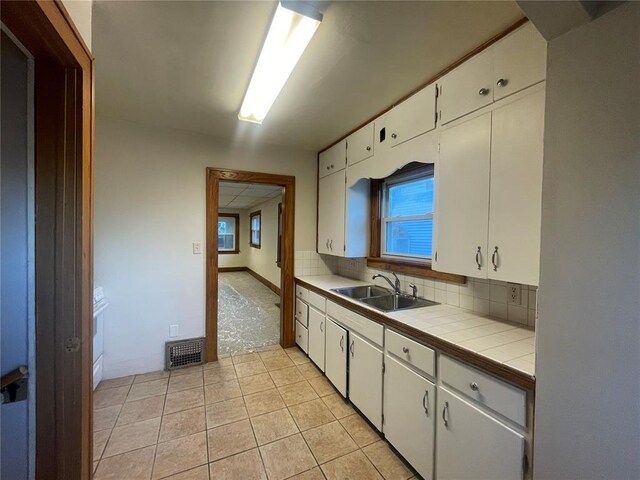 kitchen with light tile patterned floors, visible vents, white cabinets, a sink, and tile counters