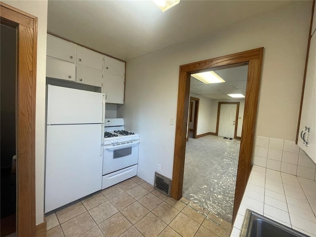 kitchen with white appliances, light tile patterned floors, white cabinetry, visible vents, and tile countertops