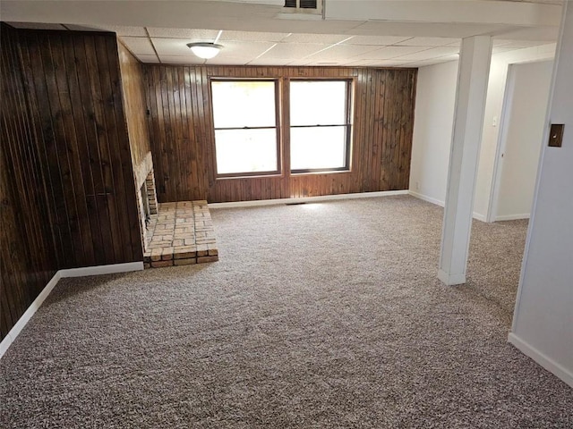 1025 Pawnee Dr NW, Cedar Rapids, IA 52405 - unfurnished living room featuring wooden walls, a drop ceiling, carpet floors, baseboards, and a stone fireplace