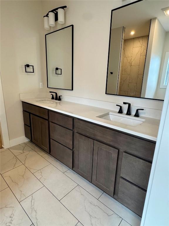 full bath with double vanity, marble finish floor, baseboards, and a sink