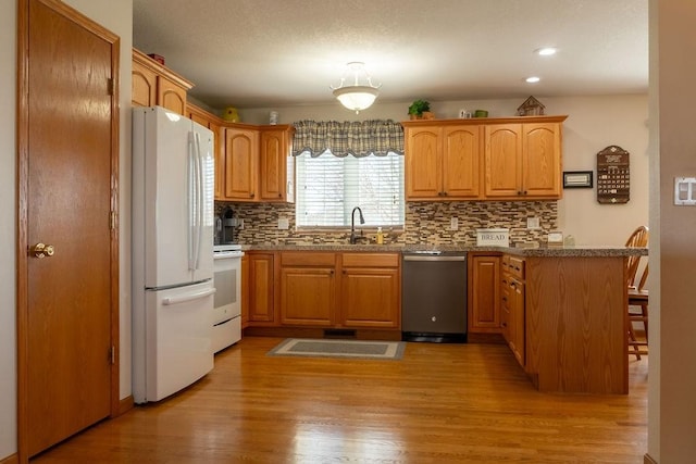 kitchen with a sink, white appliances, a peninsula, light wood-style floors, and backsplash