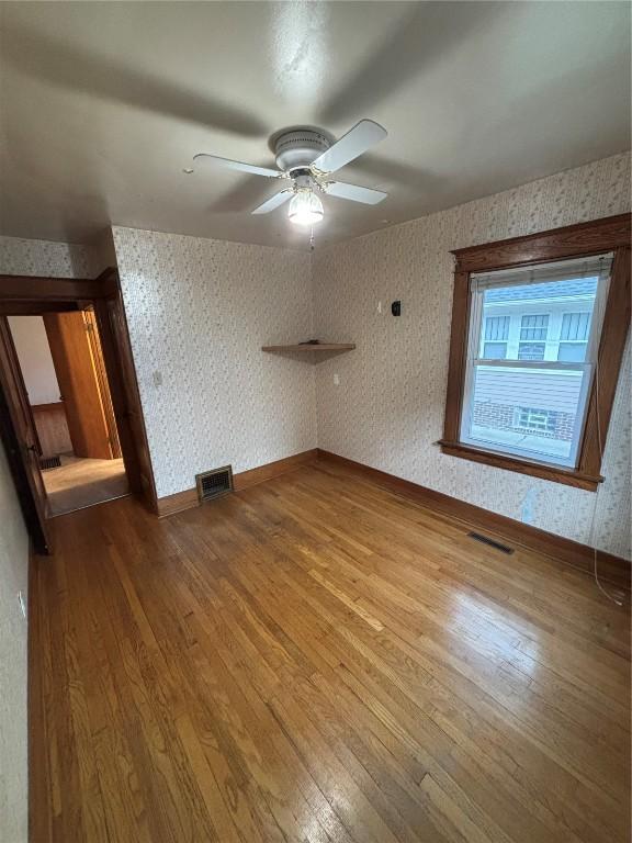 832 Daniels St NE, Cedar Rapids, IA 52402 - unfurnished room with wood finished floors, wallpapered walls, a ceiling fan, and baseboards