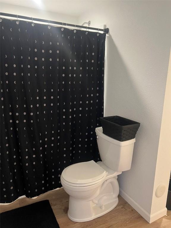 bathroom featuring curtained shower, baseboards, toilet, and wood finished floors
