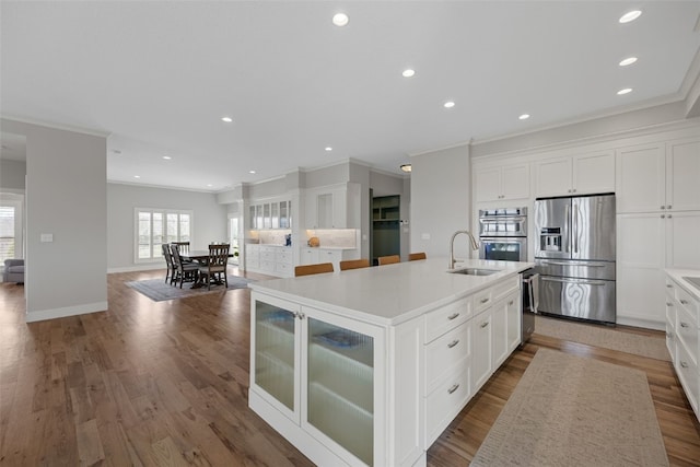 kitchen with white cabinetry, ornamental molding, a kitchen island with sink, a sink, and stainless steel appliances