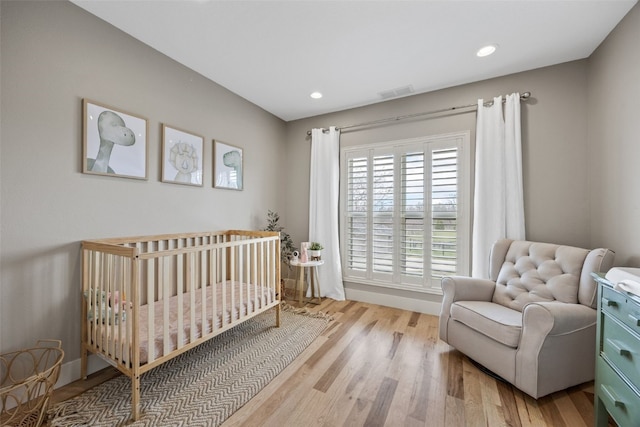 bedroom with visible vents, recessed lighting, a crib, and wood finished floors