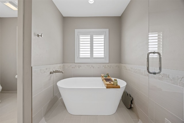 full bathroom with tile walls, a freestanding tub, tile patterned flooring, and a wainscoted wall