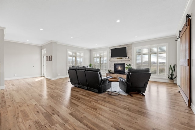 living area featuring a barn door, light wood-style flooring, a stone fireplace, and crown molding