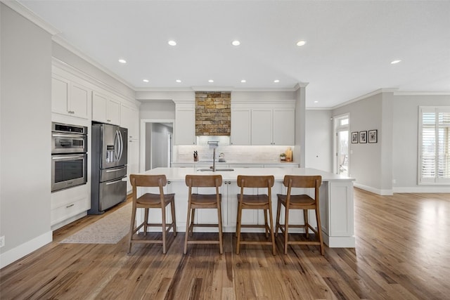 kitchen featuring crown molding, light wood-style flooring, tasteful backsplash, recessed lighting, and appliances with stainless steel finishes