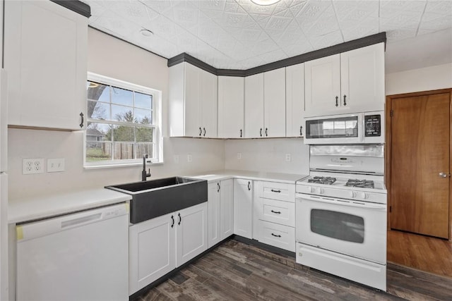 kitchen with light countertops, dark wood-type flooring, a sink, and white appliances