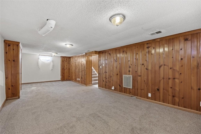 finished below grade area featuring a textured ceiling, visible vents, wood walls, stairway, and light carpet