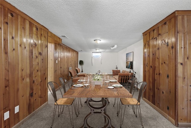 carpeted dining space with a textured ceiling, wood walls, baseboards, and visible vents