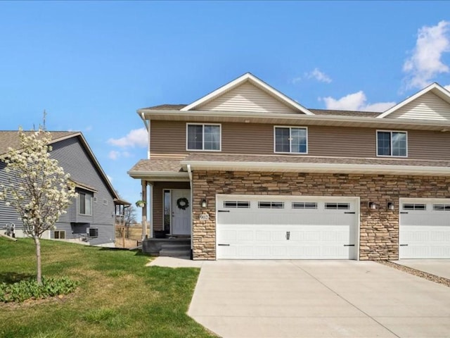 view of front facade featuring a front yard, an attached garage, stone siding, and concrete driveway