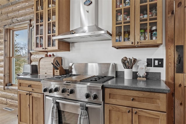 kitchen featuring dark countertops, wall chimney range hood, visible vents, stainless steel stove, and glass insert cabinets