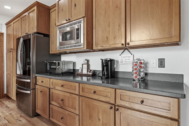 kitchen featuring recessed lighting, stainless steel appliances, dark countertops, light wood-type flooring, and brown cabinetry