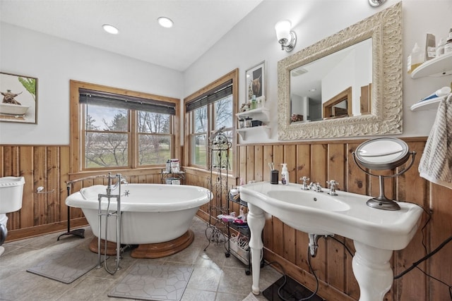 full bath with recessed lighting, lofted ceiling, wood walls, a freestanding bath, and wainscoting