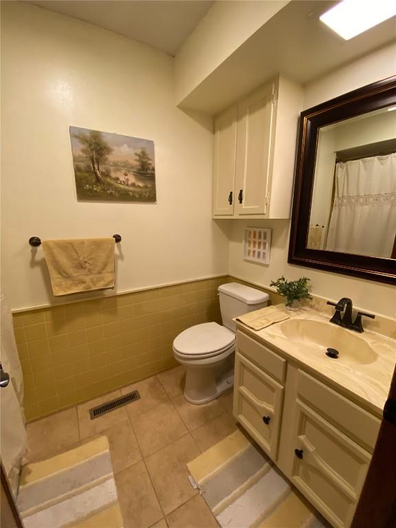 full bath with tile walls, wainscoting, toilet, tile patterned flooring, and vanity