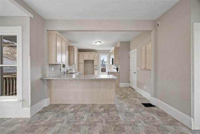 kitchen with a peninsula, light brown cabinets, a sink, light countertops, and baseboards