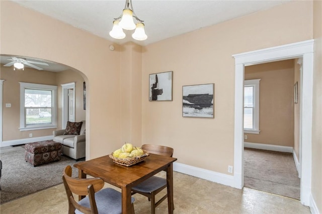 dining space with arched walkways, a wealth of natural light, baseboards, and ceiling fan with notable chandelier