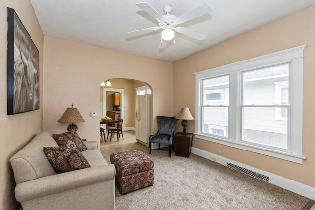 carpeted living room with arched walkways, visible vents, baseboards, and ceiling fan