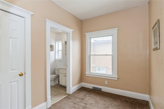 unfurnished bedroom featuring ensuite bath, visible vents, baseboards, and light carpet