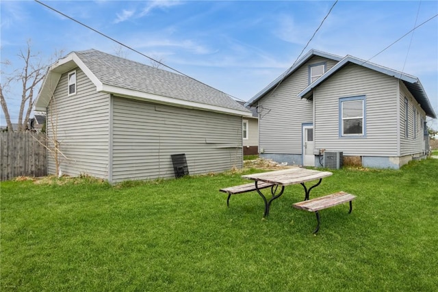 rear view of property with fence, a lawn, roof with shingles, and central AC unit