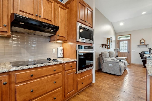 kitchen featuring under cabinet range hood, stainless steel appliances, lofted ceiling, brown cabinets, and decorative backsplash